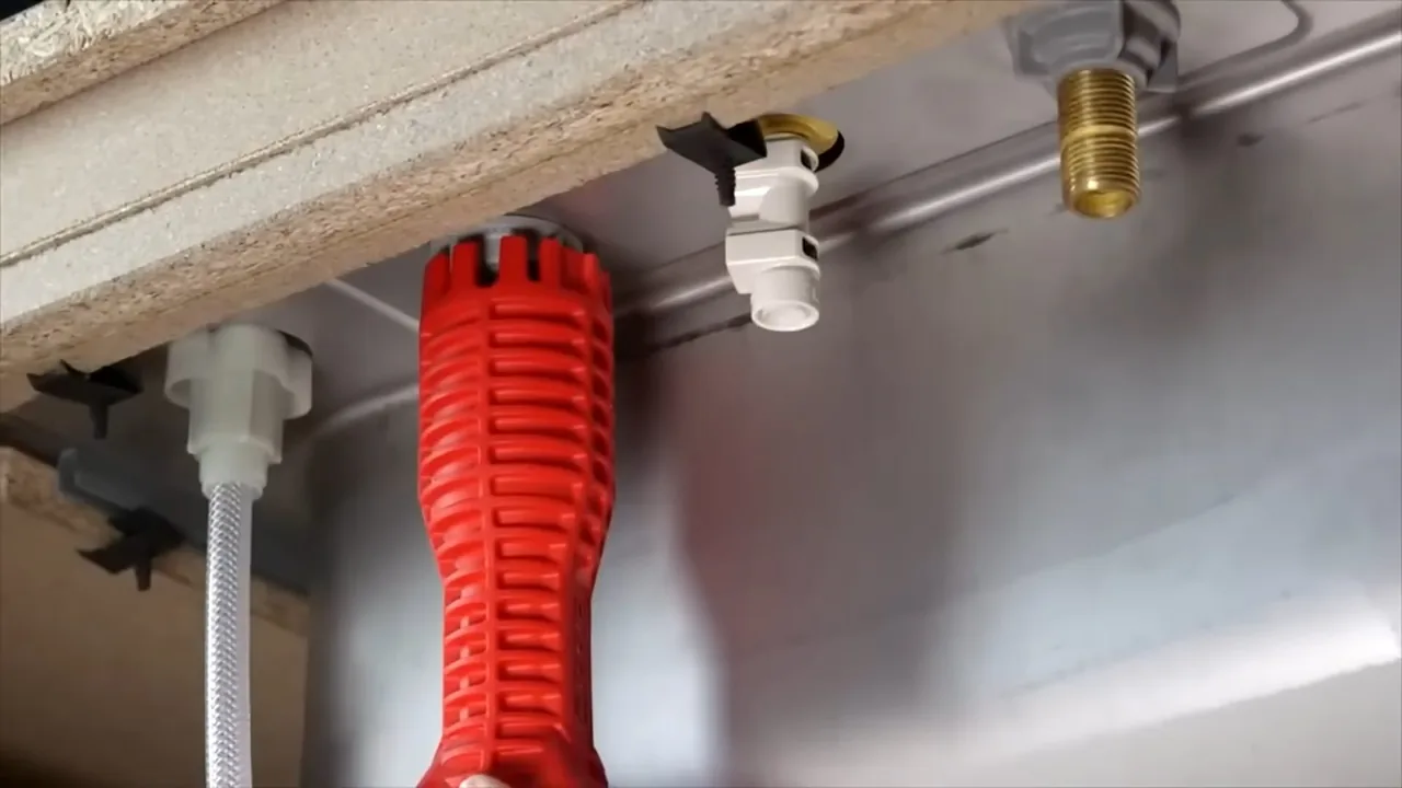 The underside of a kitchen sink showing supply connections and a red basin wrench.