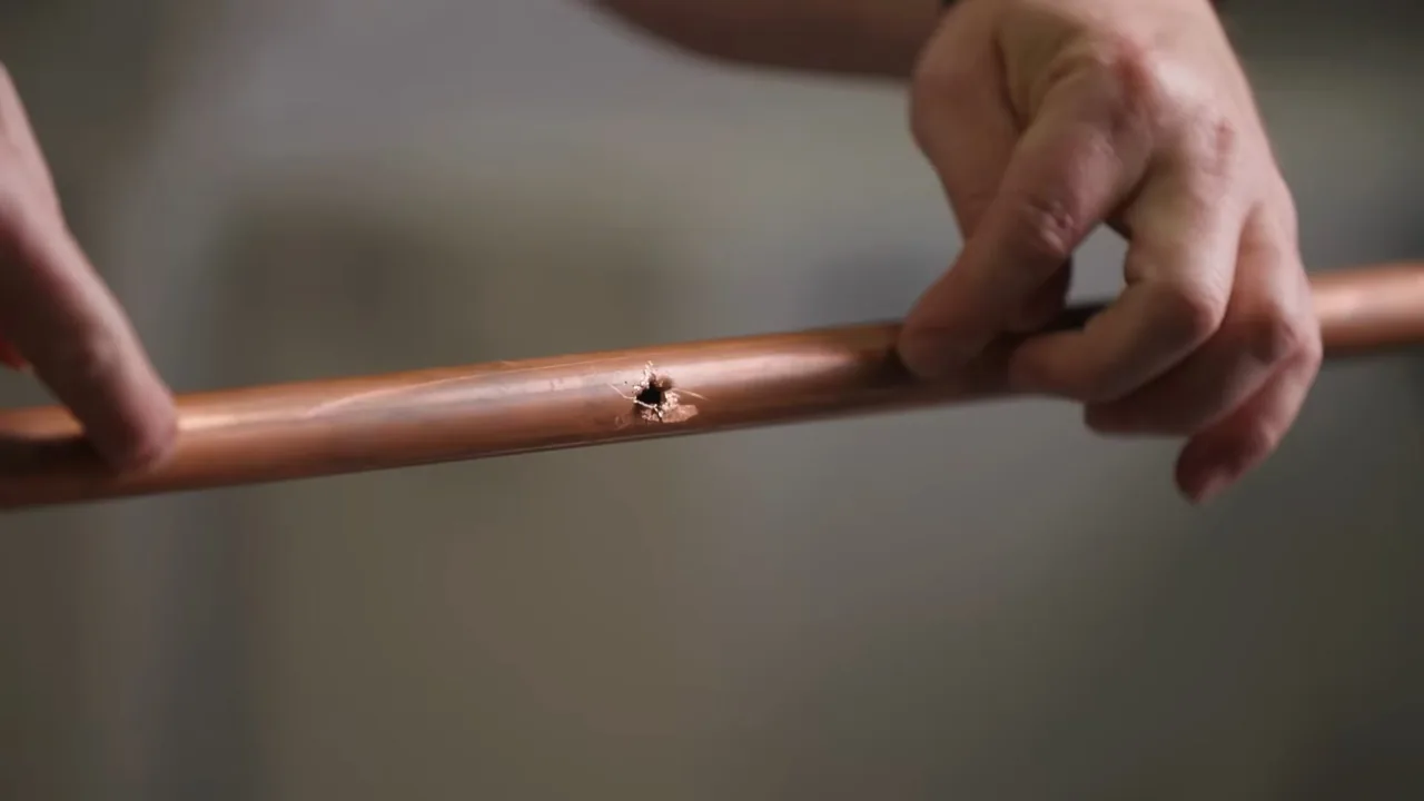 Two hands holding a section of copper pipe with a small split in its wall.