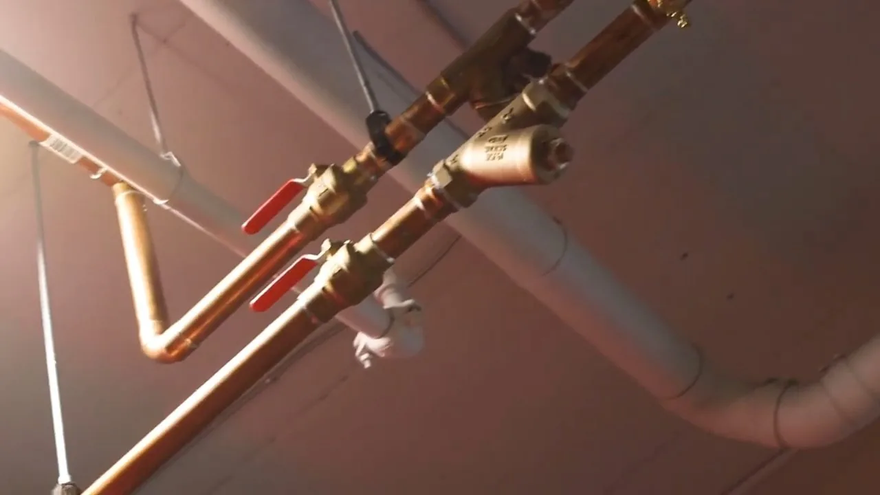 Copper supply lines with red-handled valves and a pink drain pipe running along an exposed commercial ceiling.