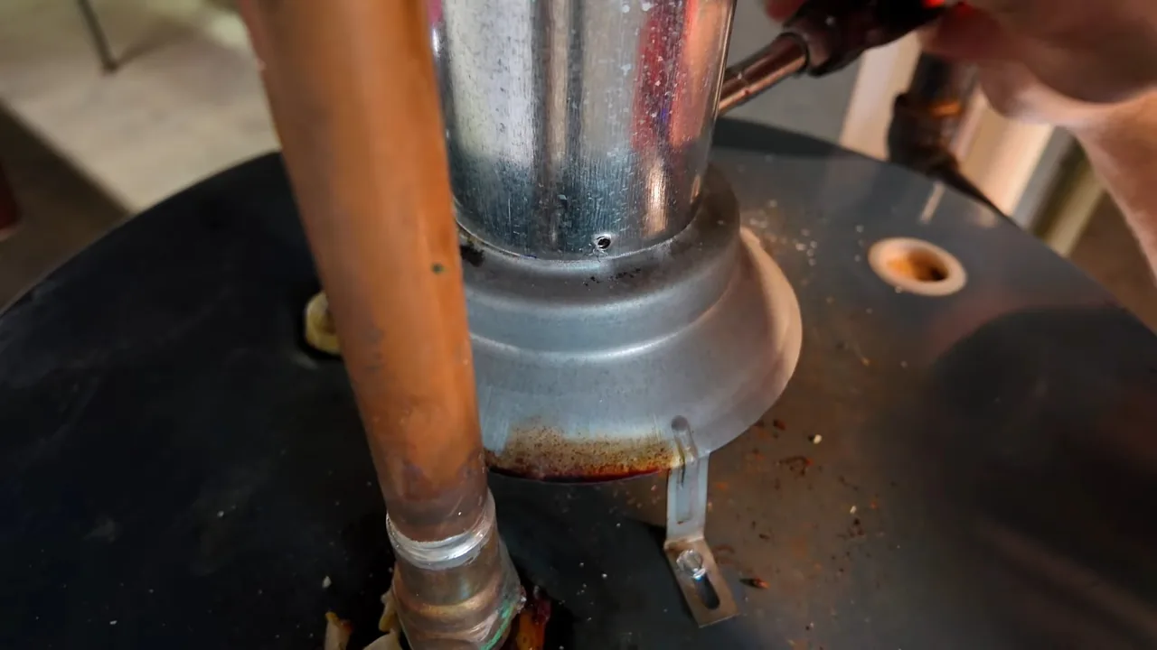 A galvanized flue collar and a copper line on top of a black water heater tank.