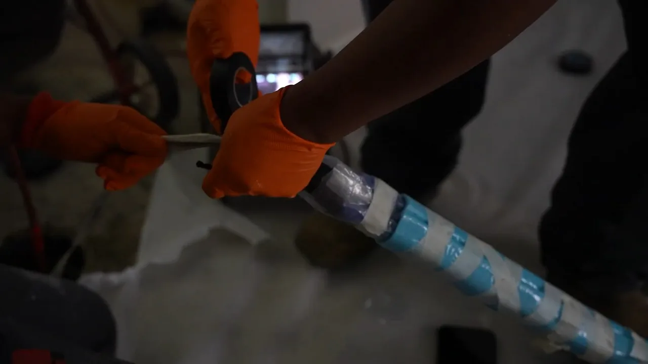 Gloved hands guiding a blue-striped liner tube along a pipe laid on a white sheet.