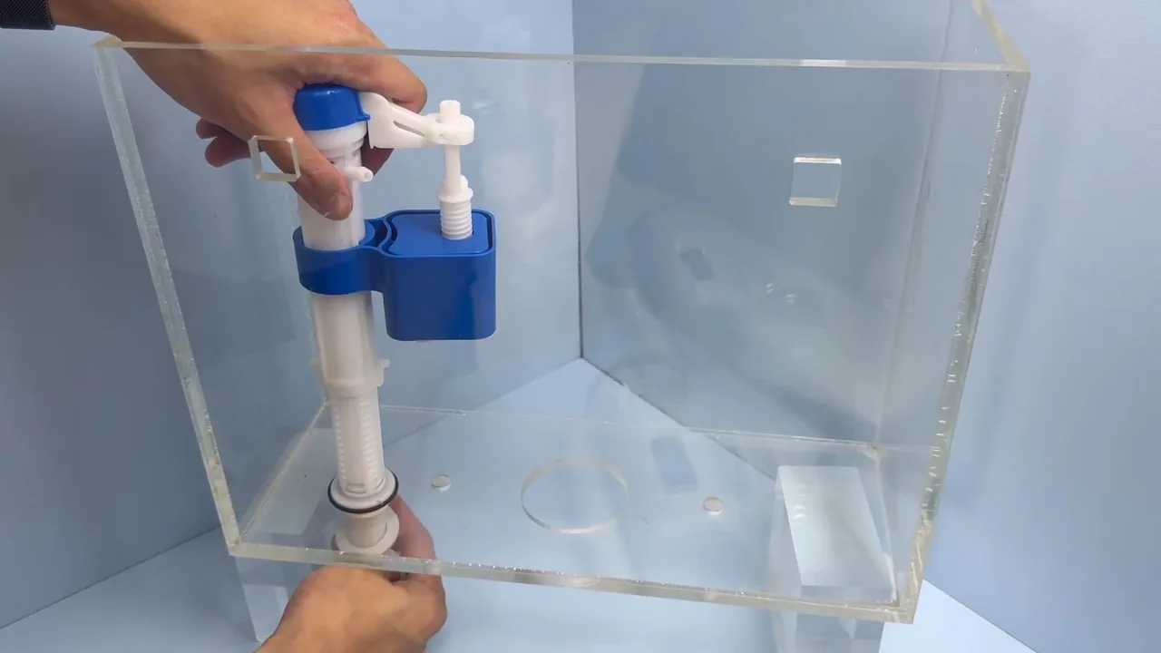 A hand adjusting a float-style fill valve inside a clear acrylic toilet tank.