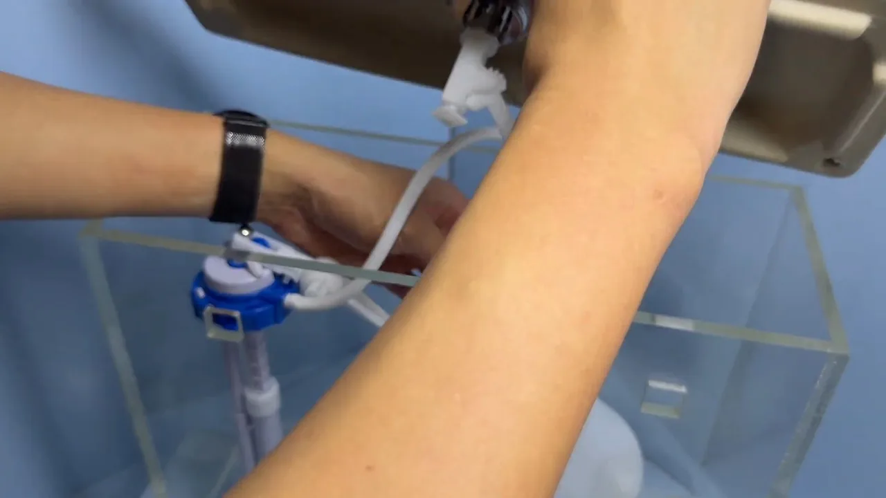 A hand adjusting the fill valve inside a clear demonstration toilet tank.