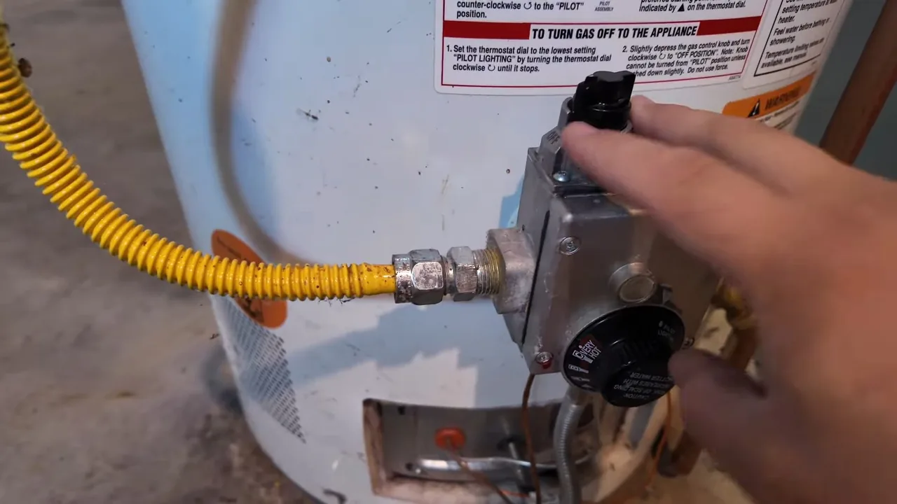 A hand at the gas control on a water heater, with a yellow corrugated gas connector running to it.