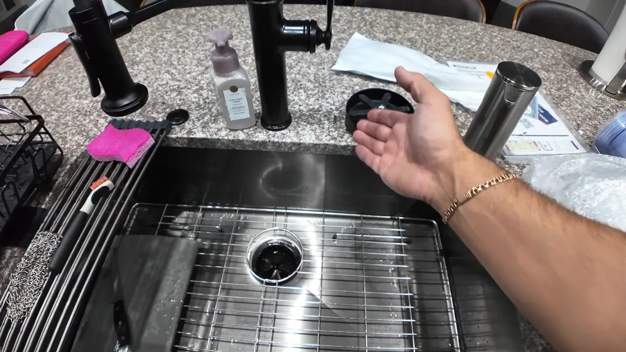 A hand over a stainless kitchen sink with a drain opening and a wire rack in the basin.