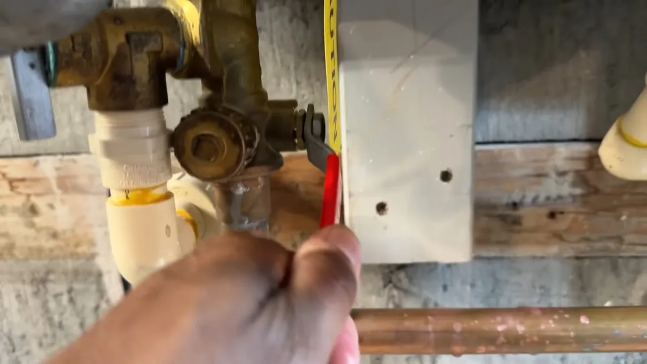 A hand using a small tool at a brass valve with white pipe beside a mounting board.