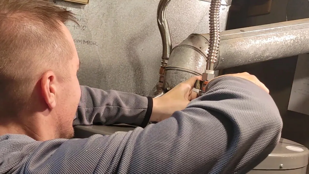 A man connecting a braided flexible connector at the top of a water heater.