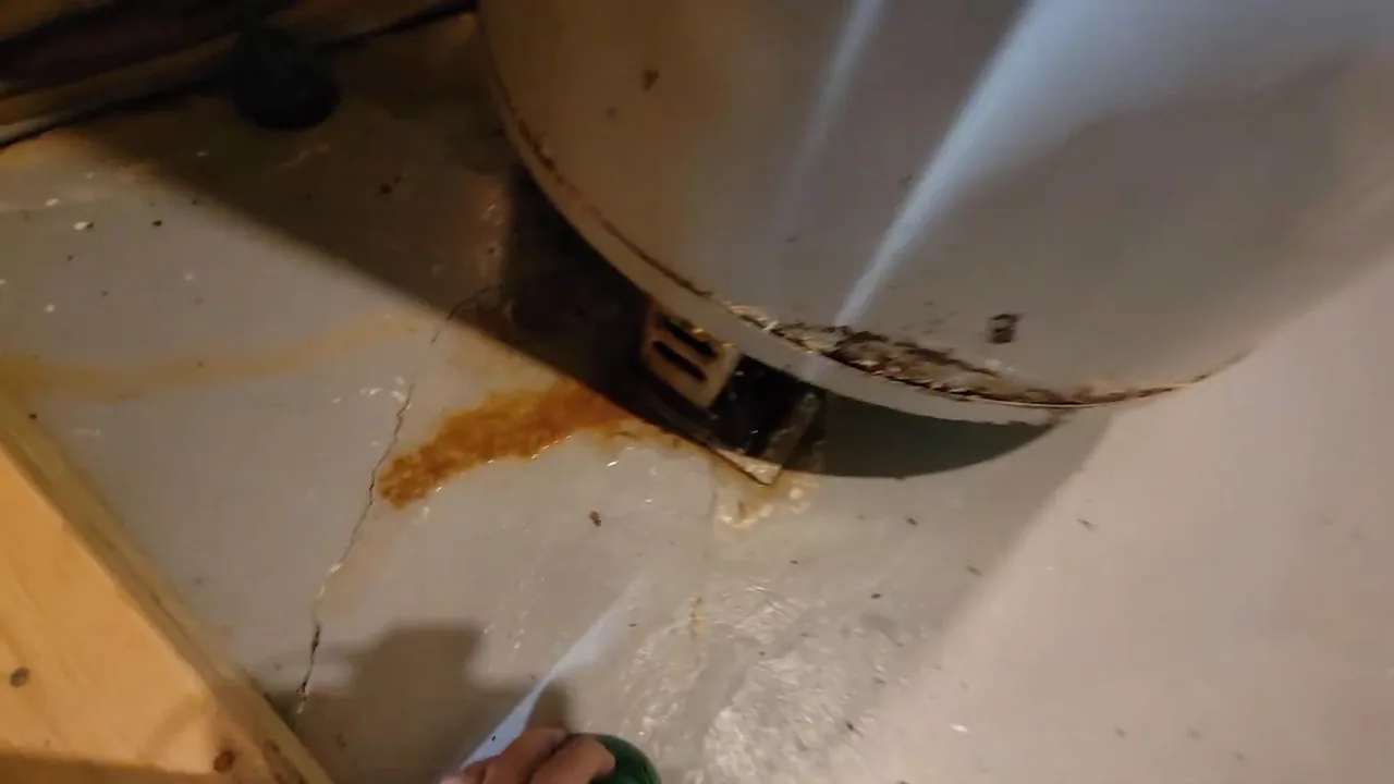 A rust-colored stain on the floor around the base of a water heater tank.