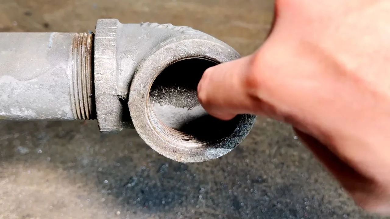 A thumb pressing at the inside of an open threaded cleanout fitting on a galvanized pipe.